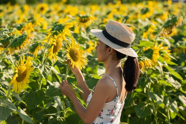 Hermosa mujer joven en un campo de girasoles con un vestido blanco. viajar en el concepto de fin de semana. retrato de mujer auténtica con sombrero de paja. Al aire libre en el campo de girasoles.