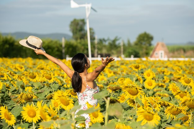 Hermosa mujer joven en un campo de girasoles con un vestido blanco. viajar en el concepto de fin de semana. retrato de mujer auténtica con sombrero de paja. Al aire libre en el campo de girasoles.