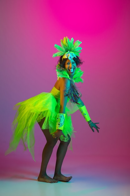 Hermosa mujer joven en carnaval, elegante disfraz de mascarada con plumas bailando en la pared degradada en neón