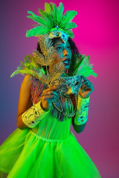 Hermosa mujer joven en carnaval, elegante disfraz de mascarada con plumas bailando en la pared degradada en neón