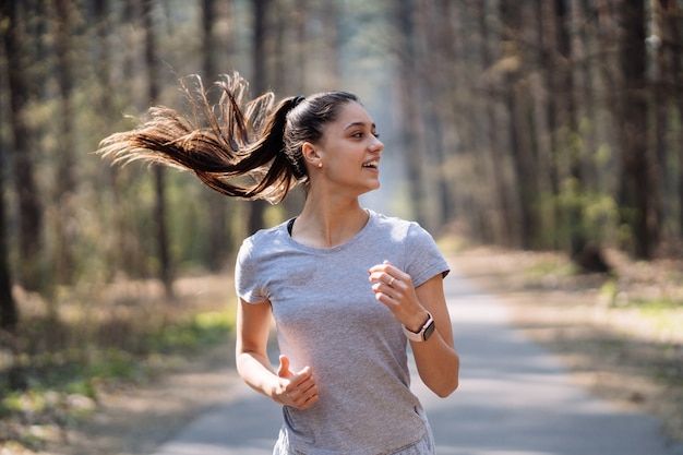 Hermosa mujer joven corriendo en el parque verde en un día soleado de verano