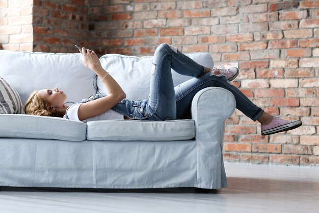Hermosa mujer joven descansando en el sofá, sala de estar interior
