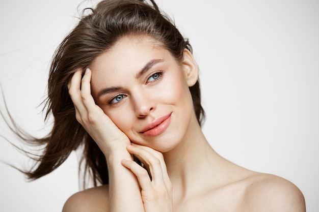 Foto gratuita hermosa mujer joven desnuda con piel limpia perfecta sonriendo tocando el pelo sobre la pared blanca. tratamiento facial.