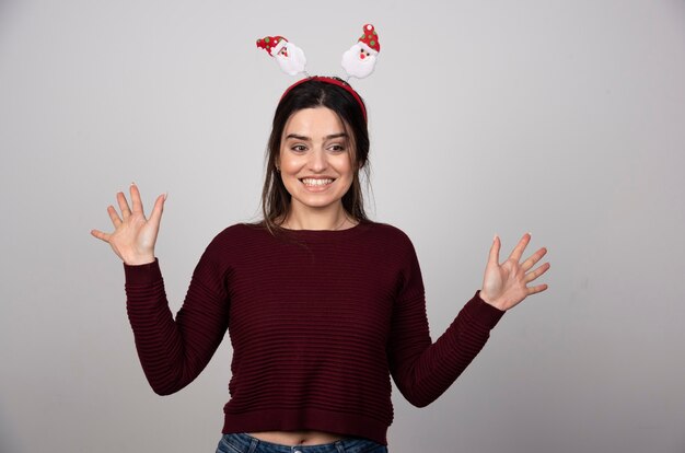 Hermosa mujer joven divertida en diadema de Navidad sobre fondo gris aislado.