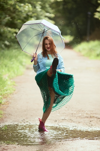 Hermosa mujer joven en falda verde se divierte caminando en botas de goma en las piscinas después de la lluvia