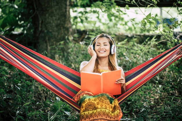 Hermosa mujer joven feliz con auriculares escuchando música y leyendo un libro
