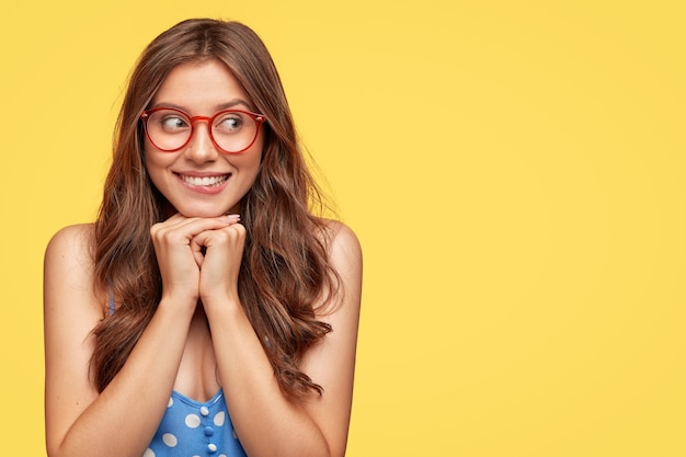 Hermosa mujer joven con gafas posando contra la pared amarilla