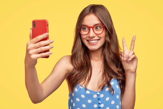 Hermosa mujer joven con gafas posando contra la pared amarilla