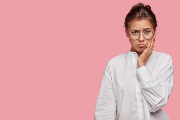 Foto gratuita hermosa mujer joven con gafas posando contra la pared rosa