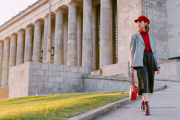 Hermosa mujer joven con gorra roja y bolso mirando a otro lado