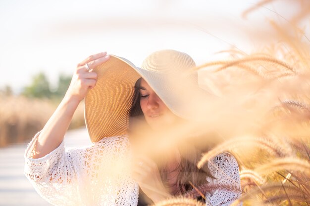 Hermosa mujer joven con un gran sombrero entre la hierba del campo de cerca.