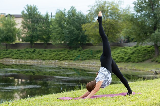 Hermosa mujer joven haciendo ejercicio de yoga en el parque verde