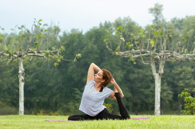 Hermosa mujer joven haciendo ejercicio de yoga en el parque verde