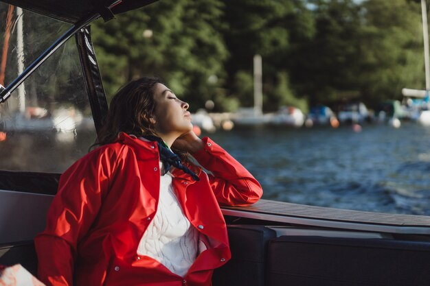 Hermosa mujer joven en un impermeable rojo monta un yate privado. Estocolmo, Suiza