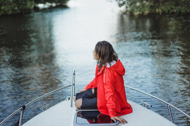 Hermosa mujer joven en un impermeable rojo monta un yate privado. Estocolmo, Suiza