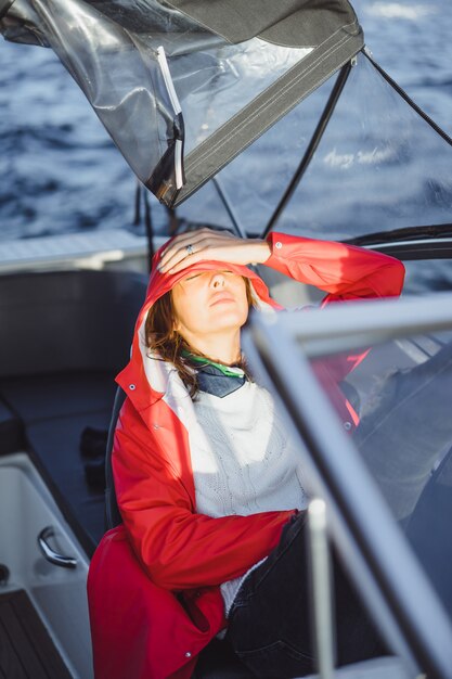 Hermosa mujer joven en un impermeable rojo monta un yate privado. Estocolmo, Suiza