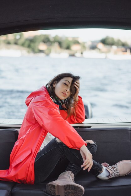Hermosa mujer joven en un impermeable rojo monta un yate privado. Estocolmo, Suiza