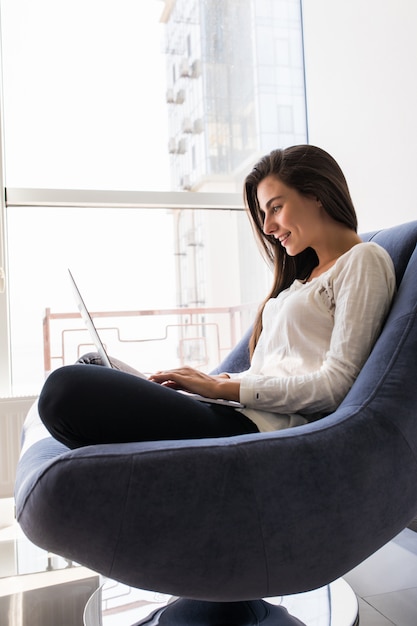 Hermosa mujer joven con laptop sentada en la silla en casa