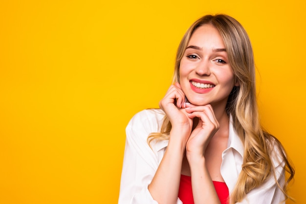 Hermosa mujer joven con la mano en la barbilla, sonriendo, en la pared amarilla.