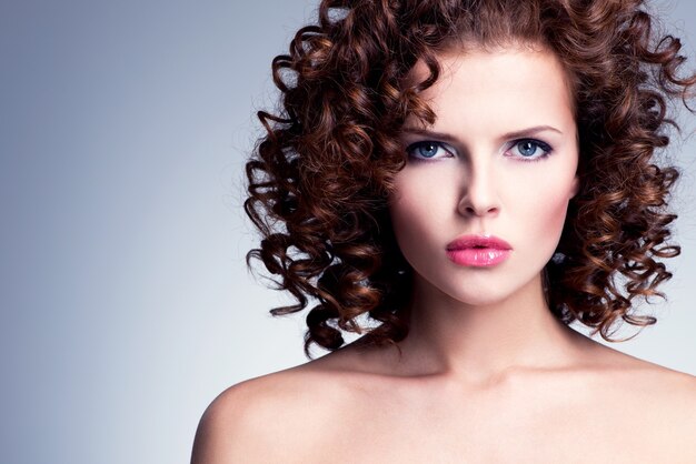 Hermosa mujer joven con maquillaje brillante. Modelo posando sobre pared gris.