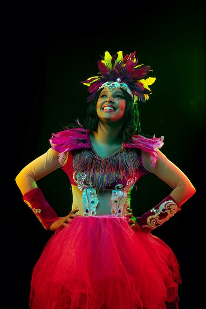 Hermosa mujer joven en máscara de carnaval y disfraz de mascarada en luces de colores