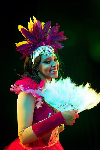 Hermosa mujer joven en máscara de carnaval y disfraz de mascarada en luces de colores