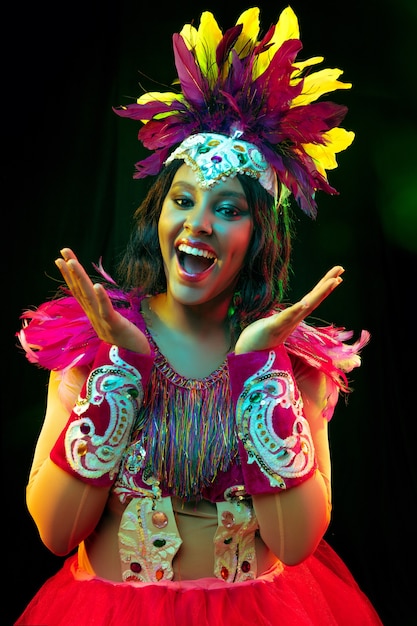 Hermosa mujer joven en máscara de carnaval y disfraz de mascarada en luces de colores