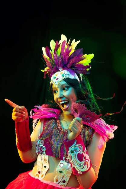 Hermosa mujer joven en máscara de carnaval y disfraz de mascarada en luces de colores