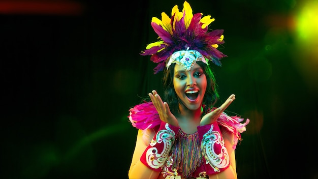 Hermosa mujer joven en máscara de carnaval, elegante traje de mascarada con plumas y bengalas invitando