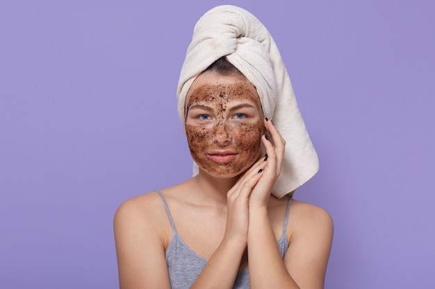 Hermosa mujer joven con máscara de chocolate en la cara, posa con una toalla blanca en la cabeza