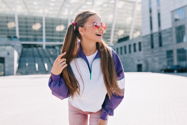 Hermosa mujer joven de moda en ropa elegante con gafas de sol rosas y riendo