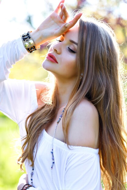 Hermosa mujer joven con pelo largo, vestido de luz blanca disfrutando de un día soleado de primavera en el jardín sobre fondo floreciente de sakura. Modelo elegante, relajante, soñador, emociones verdaderas, sentimientos frescos.