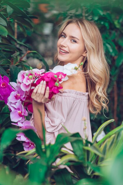 Hermosa mujer joven de pie cerca de las plantas con ramas de orquídea