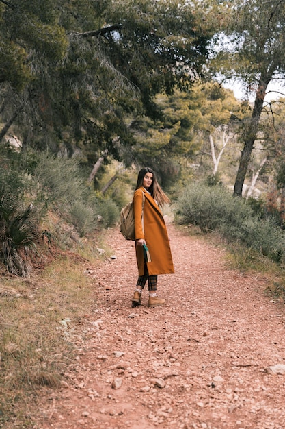 Hermosa mujer joven de pie en el sendero de montaña con libro en mano