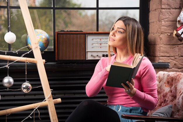 Hermosa mujer joven posando con libro en casa.