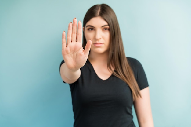 Hermosa mujer joven que muestra un gesto de parada con la mano mientras hace contacto visual en el estudio