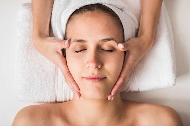 Foto gratuita hermosa mujer joven que recibe un masaje facial con los ojos cerrados en un salón de spa