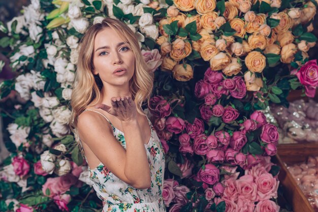 Hermosa mujer joven que sopla un beso de pie contra el fondo rosa