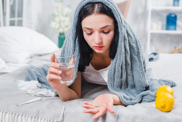 Hermosa mujer joven que sufre de fiebre con vaso de agua y pastillas en la mano