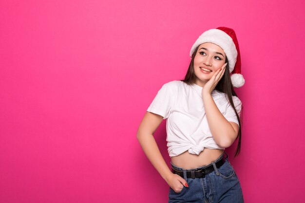 Hermosa mujer joven en rojo con sombrero de santa aislado en la pared rosa.