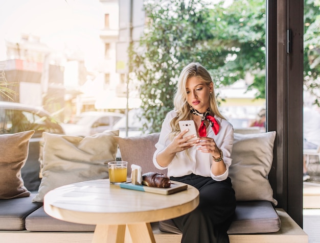 Foto gratuita hermosa mujer joven sentada en la cafetería con teléfono móvil