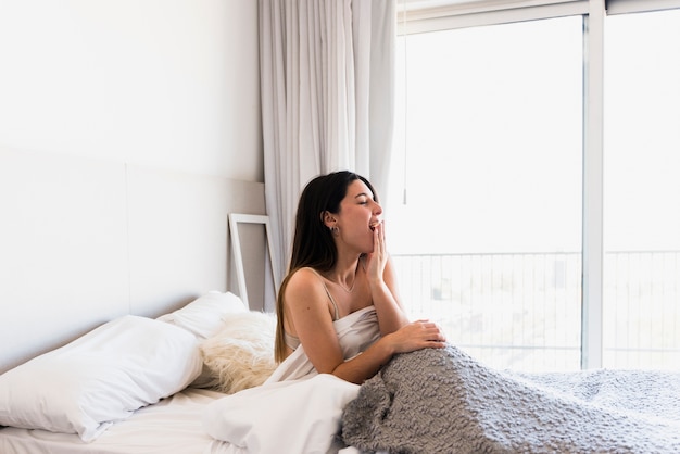 Hermosa mujer joven sentada en la cama bostezando