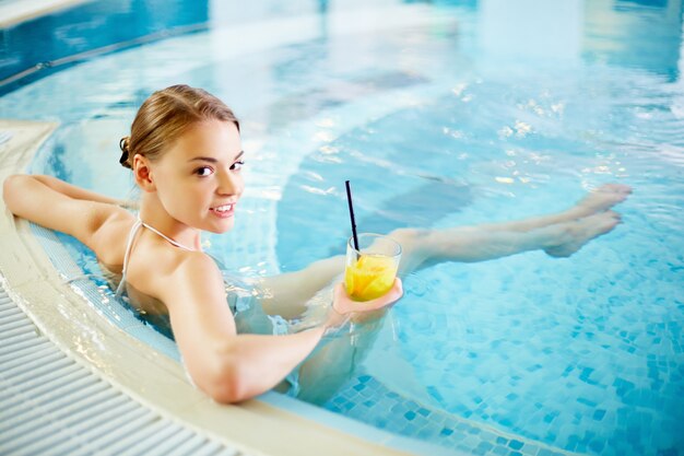 Hermosa mujer joven sentada con un cóctel en el jacuzzi