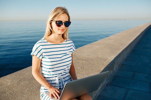 Hermosa mujer joven sentada en la playa con portátil