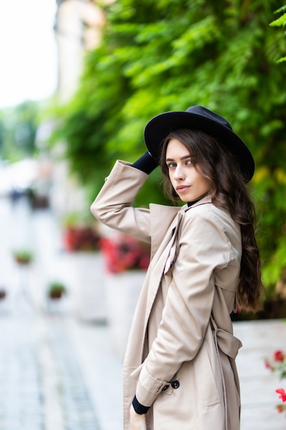 Hermosa mujer joven con sombrero y abrigo caminando en la ciudad.