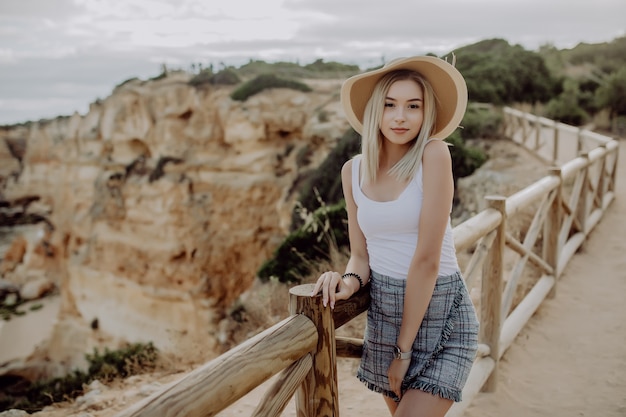 Hermosa mujer joven con sombrero de paja de pie en el punto de vista de costa con playa de piedra