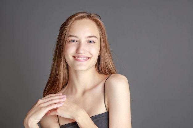 Hermosa mujer joven sonriente con el concepto de belleza natural de la cara de la piel perfecta aislada en el fondo gris del estudio