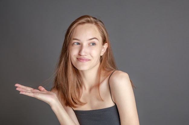 Hermosa mujer joven sonriente con el concepto de belleza natural de la cara de la piel perfecta aislada en el fondo gris del estudio