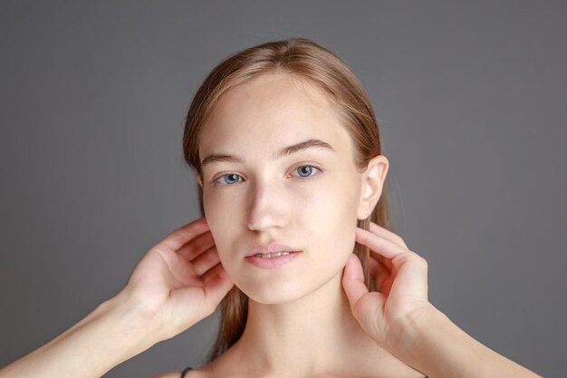 Hermosa mujer joven sonriente con el concepto de belleza natural de la cara de la piel perfecta aislada en el fondo gris del estudio