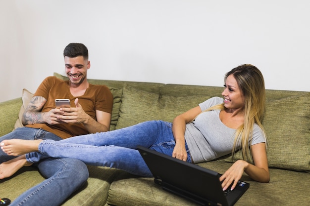 Foto gratuita hermosa mujer joven sonriente con portátil sentado cerca de su novio con smartphone